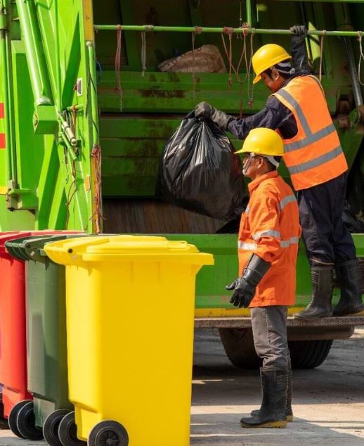A green garbage truck being loaded with trash by workers, part of a junk removal service in Chicago, IL.