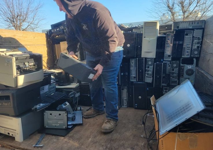 A man poses next to a heap of discarded electronics, representing an e-waste junk service in Chicago, IL.